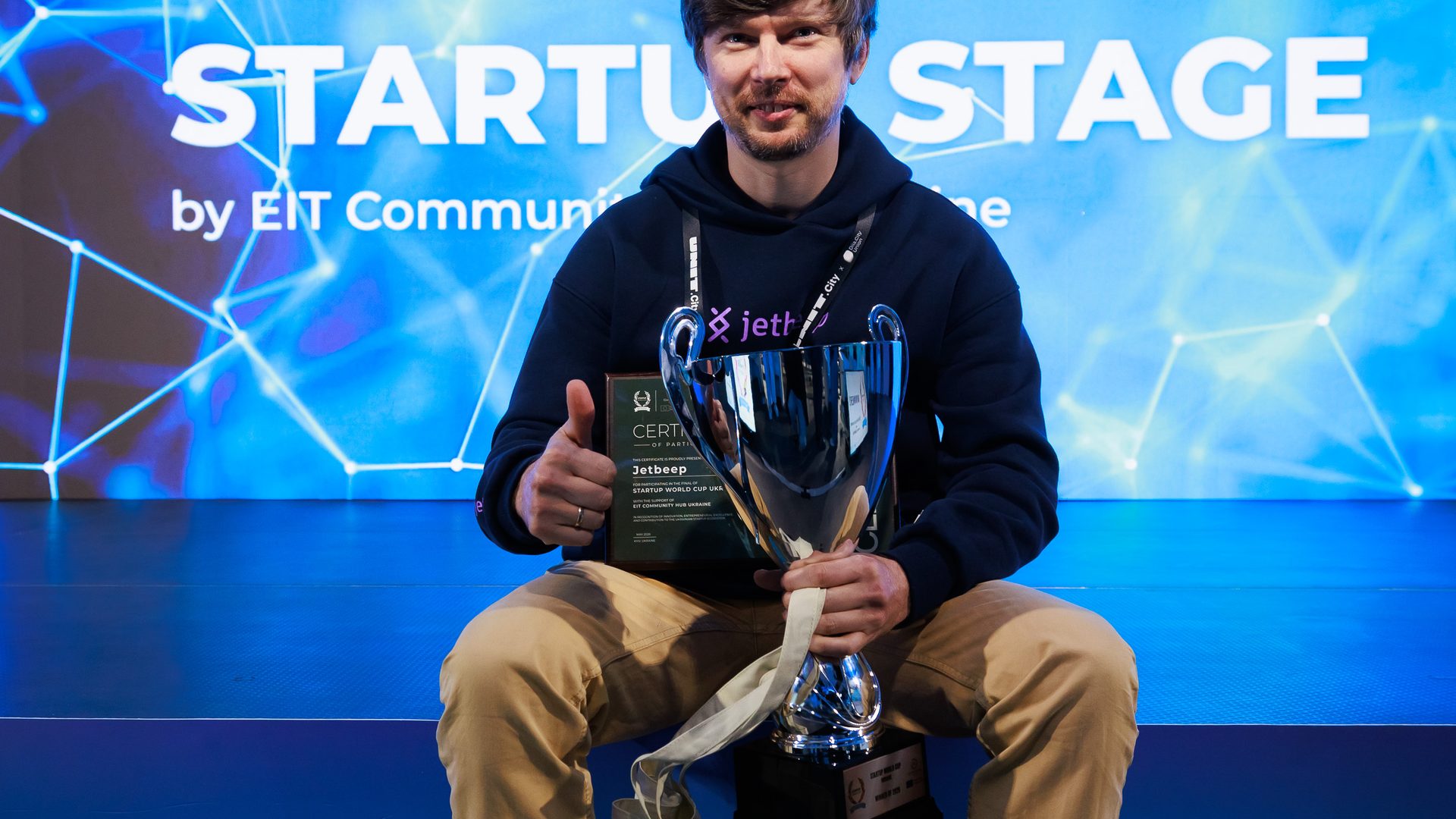 Jetbeep founder holding the Startup World Cup Ukraine 2026 trophy and certificate on the EIT Community Stage in Kyiv