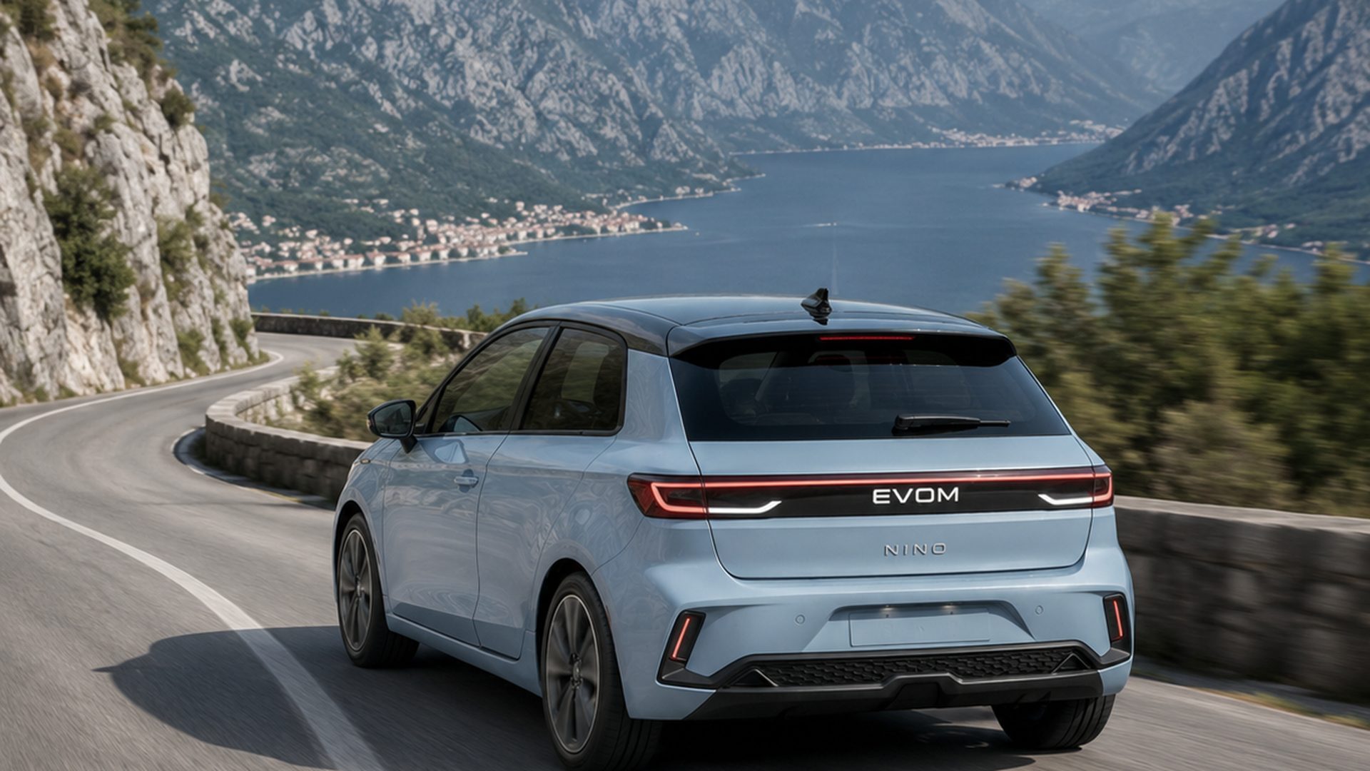 Rear three-quarter render of the EVOM electric vehicle on a coastal mountain road in Montenegro