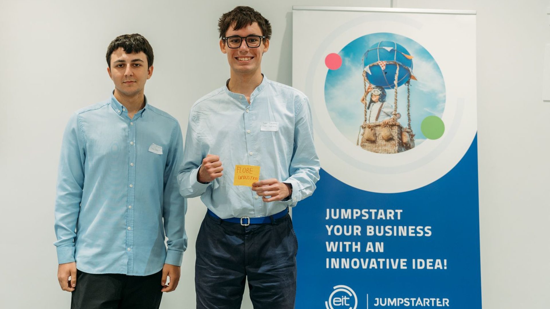 Two Flobe Industries founders holding a team sign next to an EIT Jumpstarter banner